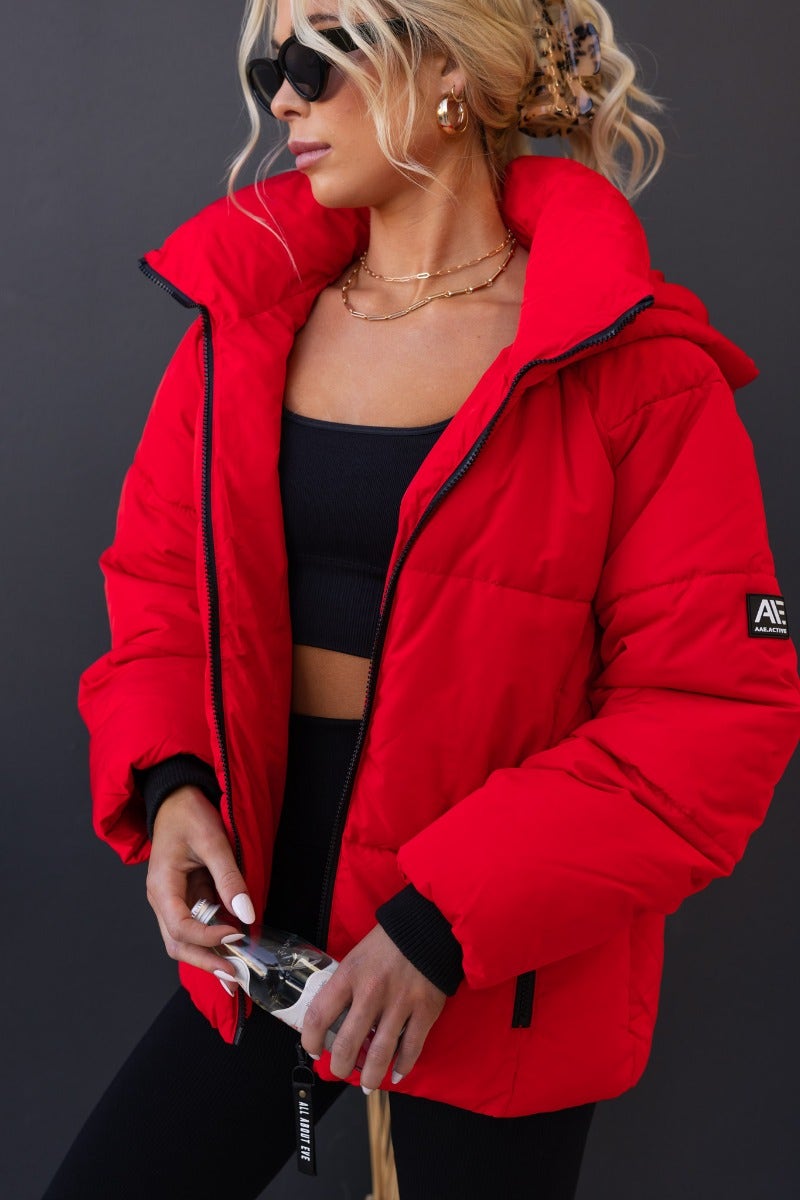 Delila Puffer Jacket in bright red with high neckline and removable hood, worn by model with stylish accessories.