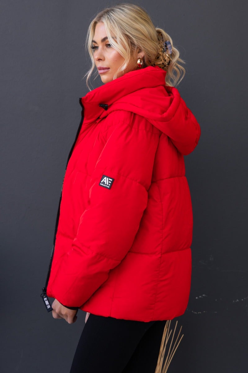 Model wearing a red Delila puffer jacket with a high neckline and removable hood, showcasing its stylish comfort.