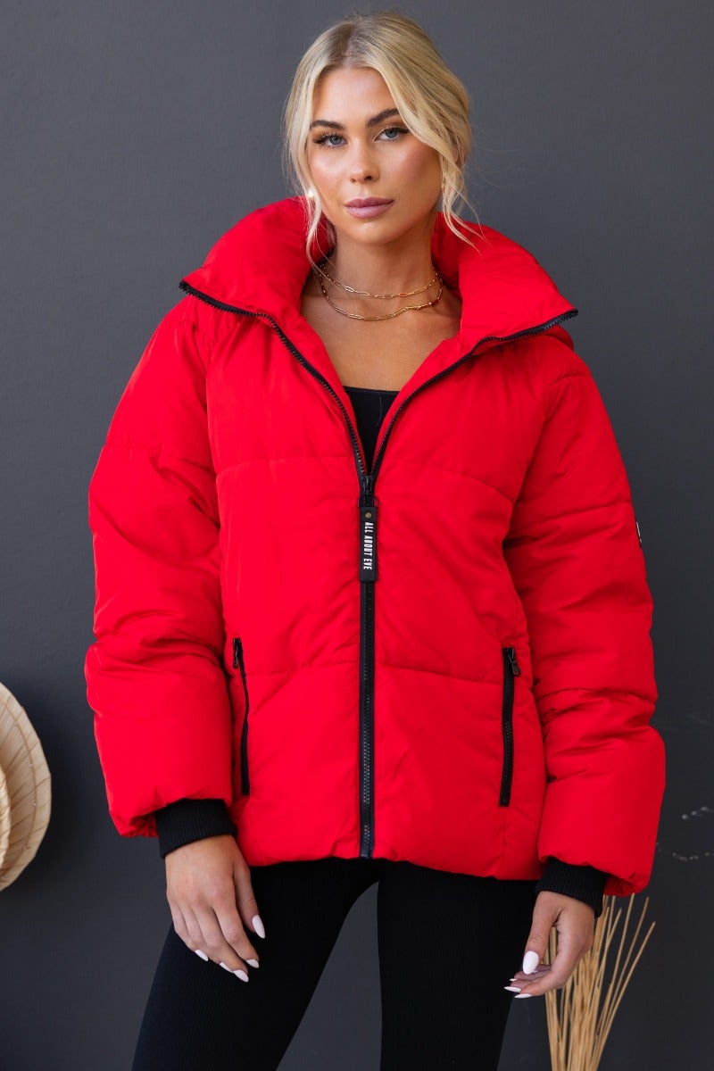 Delila Red Puffer Jacket with high neckline, removable hood, and zip-up front, worn by model, perfect for winter.