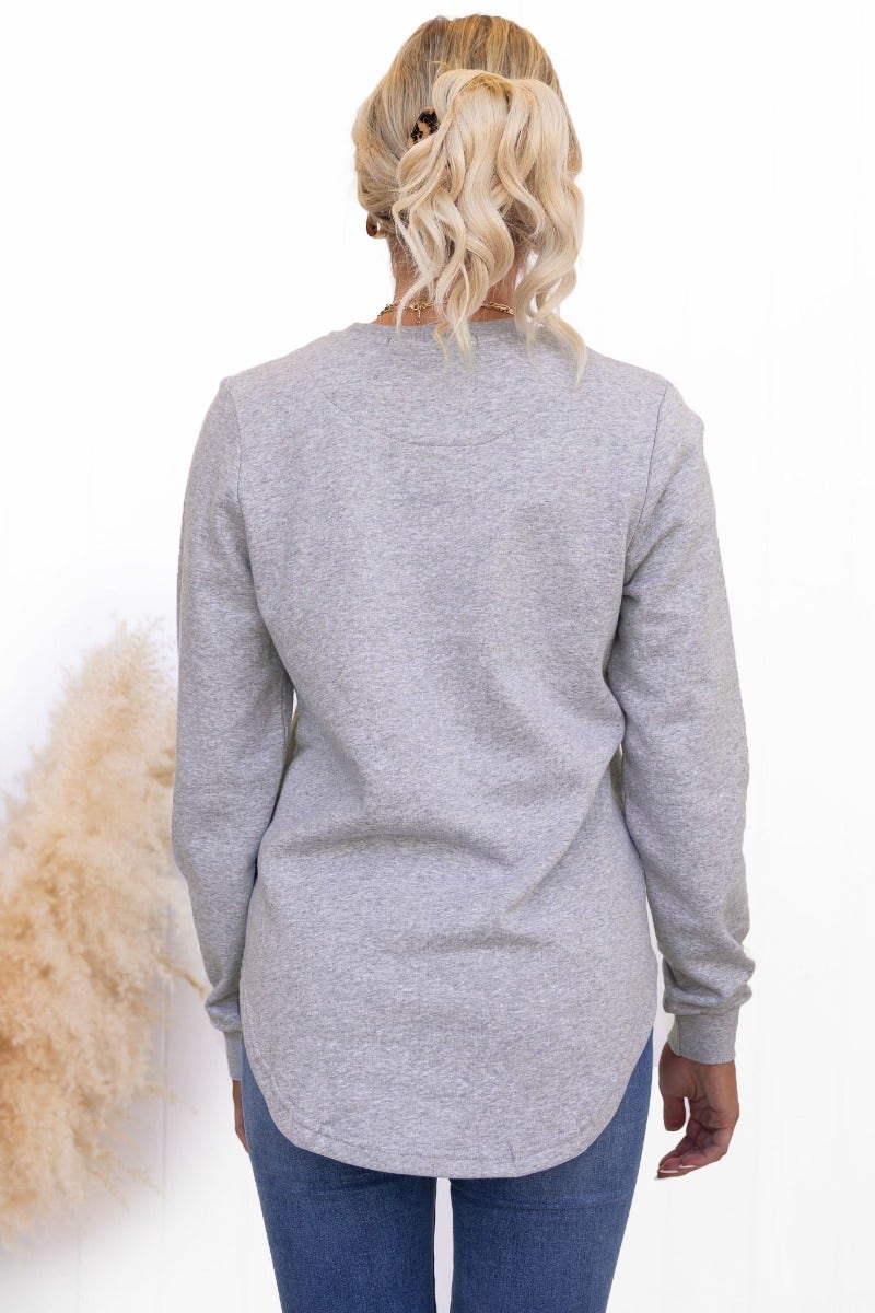 Back view of the grey Aces Jumper featuring a crew neck and scallop hemline, modeled by a woman with wavy hair.