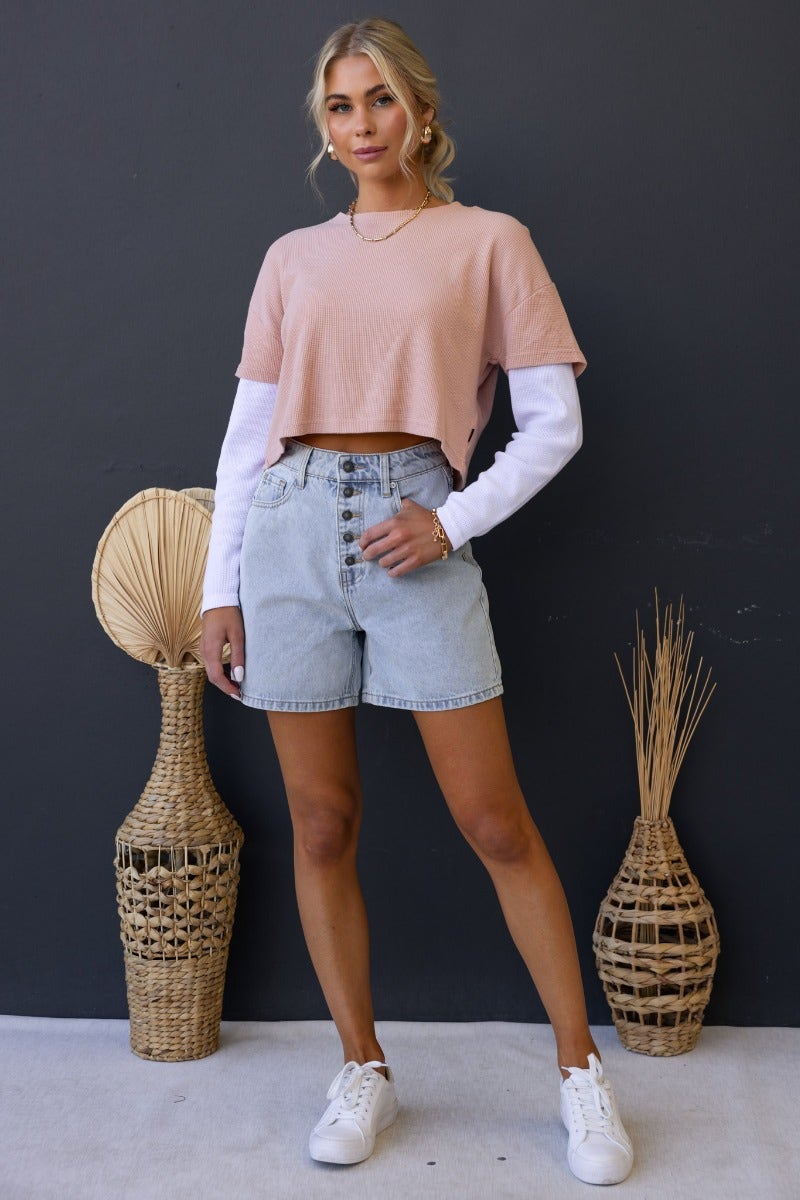 Model wearing Stazie shorts with a pink crop top and white long sleeves, showcasing denim shorts and casual footwear.