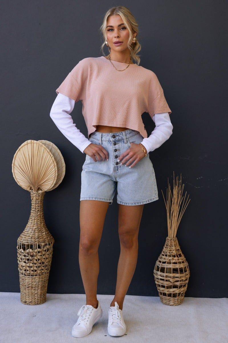 Model wearing Tyrra Top, a pink textured crop top with white sleeves, paired with high-waisted denim shorts.