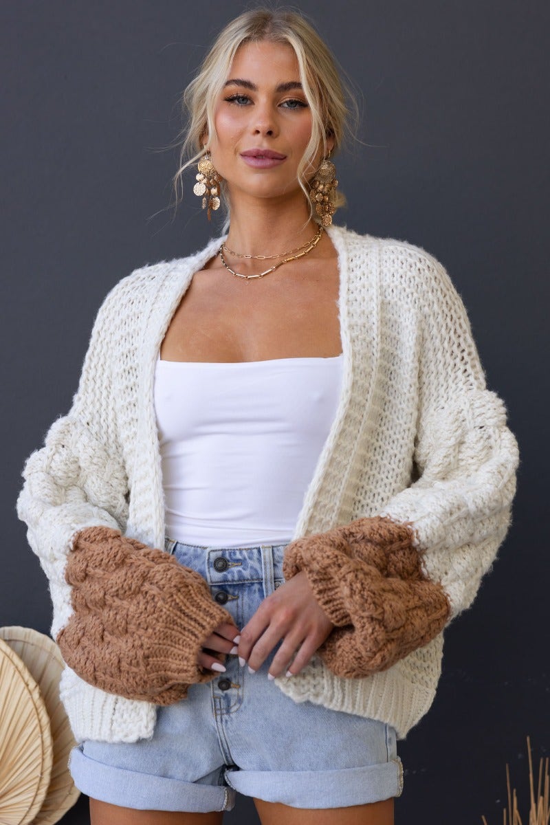 Model wearing Qira Cardigan, a knit cardigan with chunky sleeves and semi-open weave, styled with shorts.
