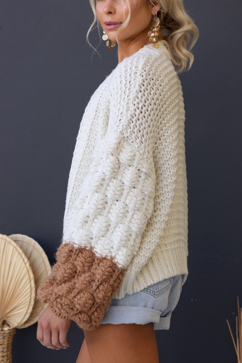 Model wearing Qira Cardigan featuring chunky sleeves and a semi-open weave, styled with shorts and accessories.