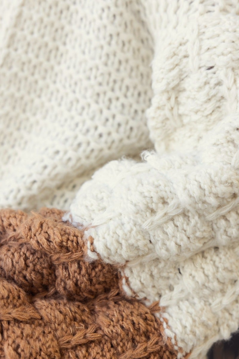 Close-up of Qira Cardigan showing semi-open weave and chunky sleeves in cream and brown colors, highlighting texture and material.