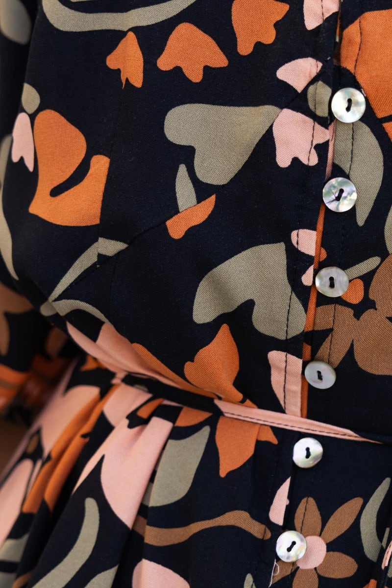 Close-up of Enver Dress featuring floral print, V-neckline, buttons, and fabric tie at waist.