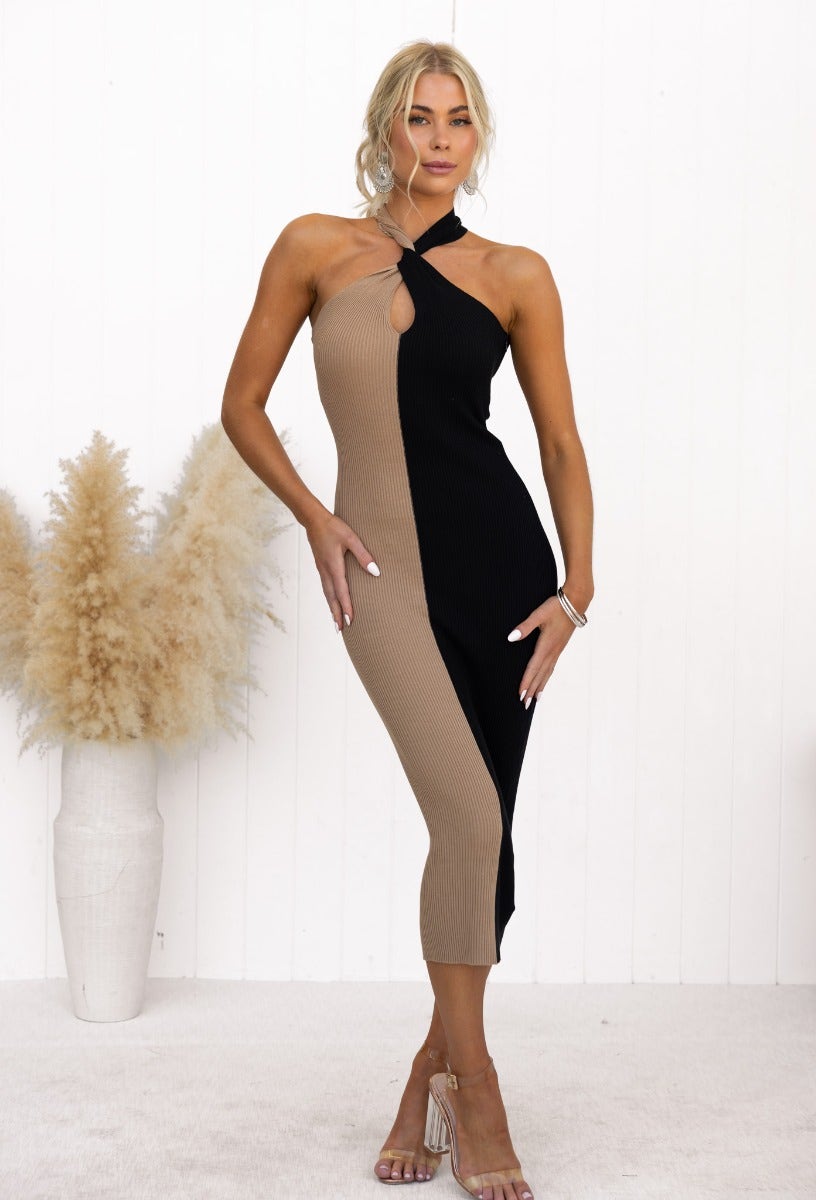 Model wearing a black and beige midi dress with a twist neckline detail and side cut, showcasing its elegant fit.