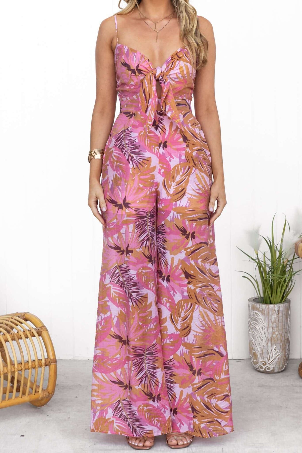 Model wearing a multicolor print Sun Dazed jumpsuit with adjustable straps and tie at bust, featuring pockets and lined design.