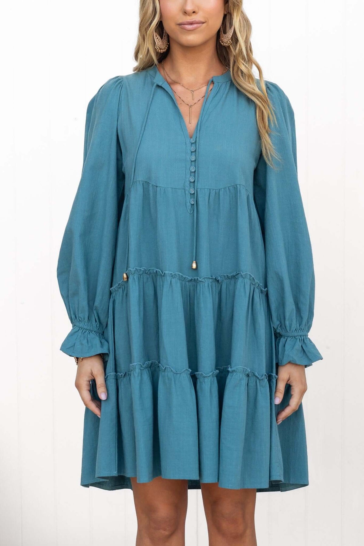 Boone Dress in teal with V-neckline, button-up front, and tiered ruffle details, worn by model.
