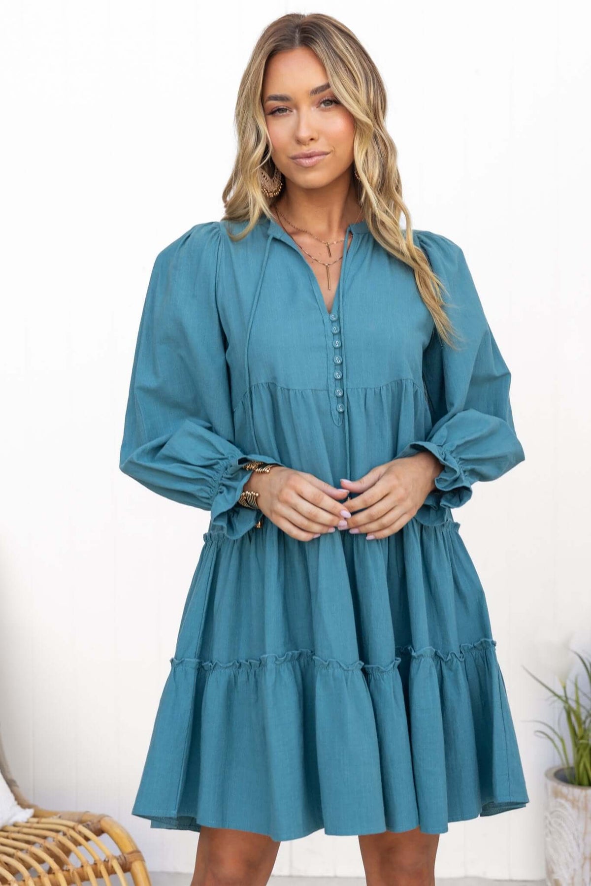 Boone Dress in teal with V-neckline, tie detail, button-up front, and ruffled hem, styled for a relaxed fit.