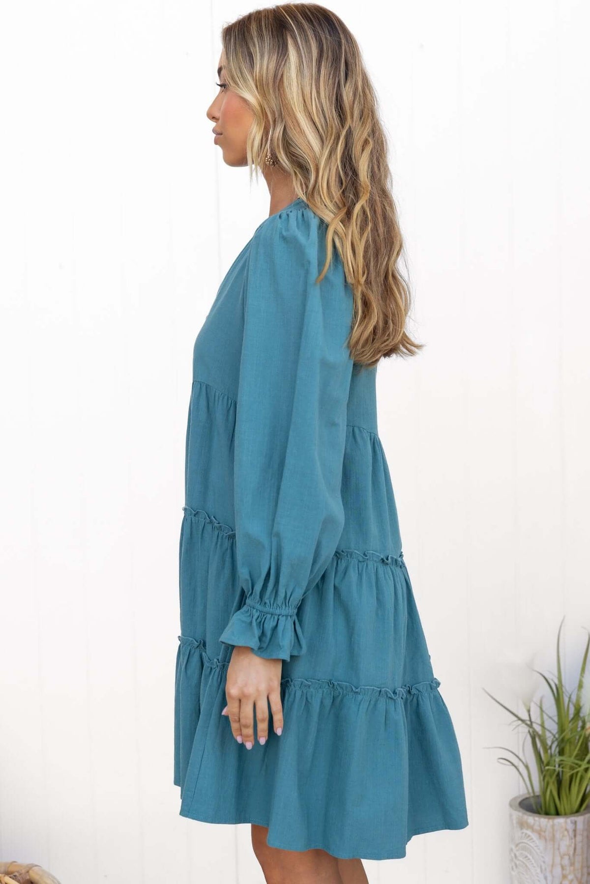Side view of a model wearing a teal Boone Dress with V-neckline and ruffled tiers.
