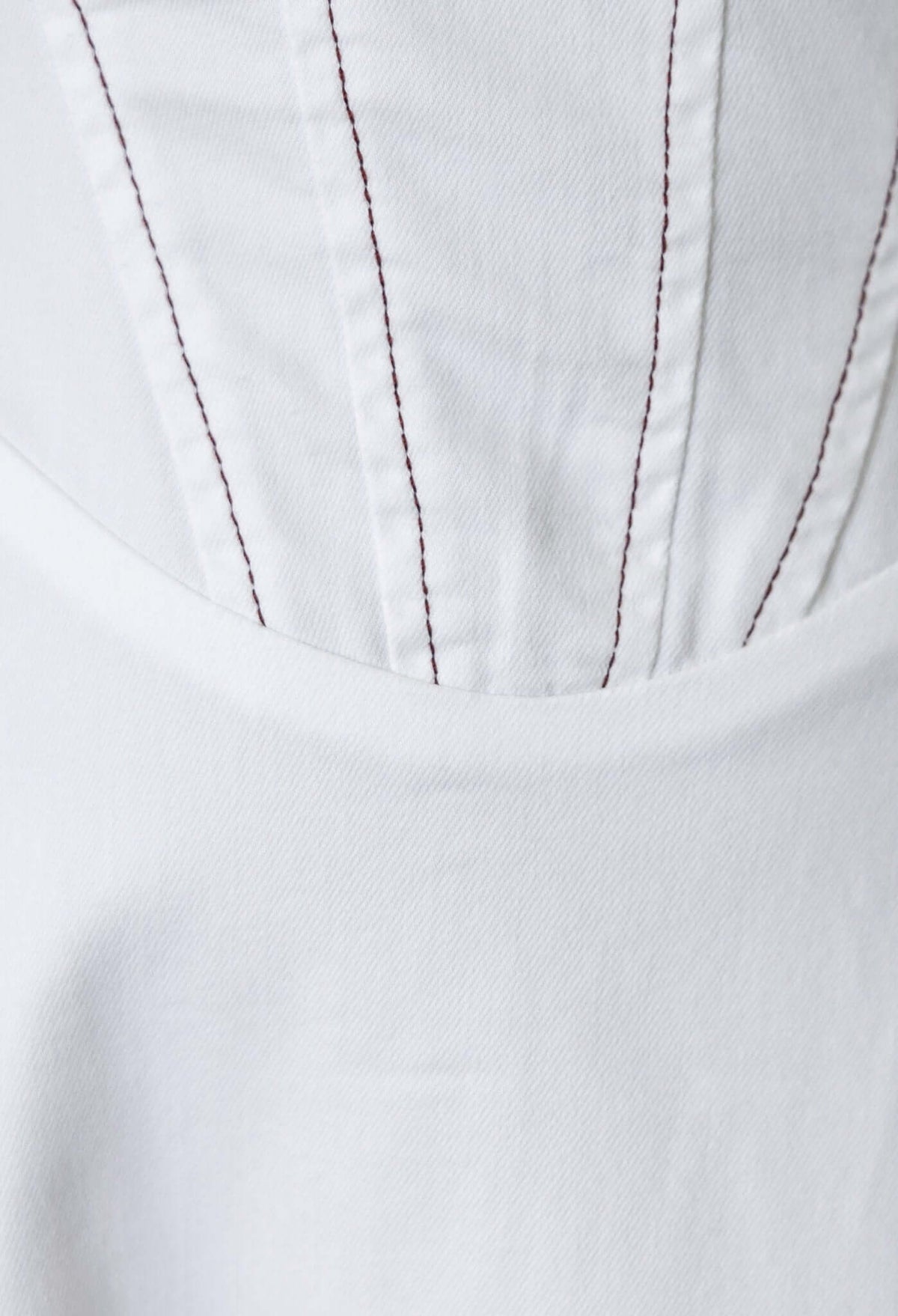 Close-up of white fabric showcasing detailed stitching on a denim midi dress, highlighting its texture and design.