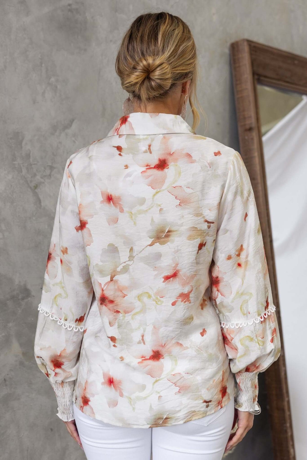 Back view of Kellee Shirt featuring floral design and elastic sleeves, paired with white pants, styled against a concrete wall.