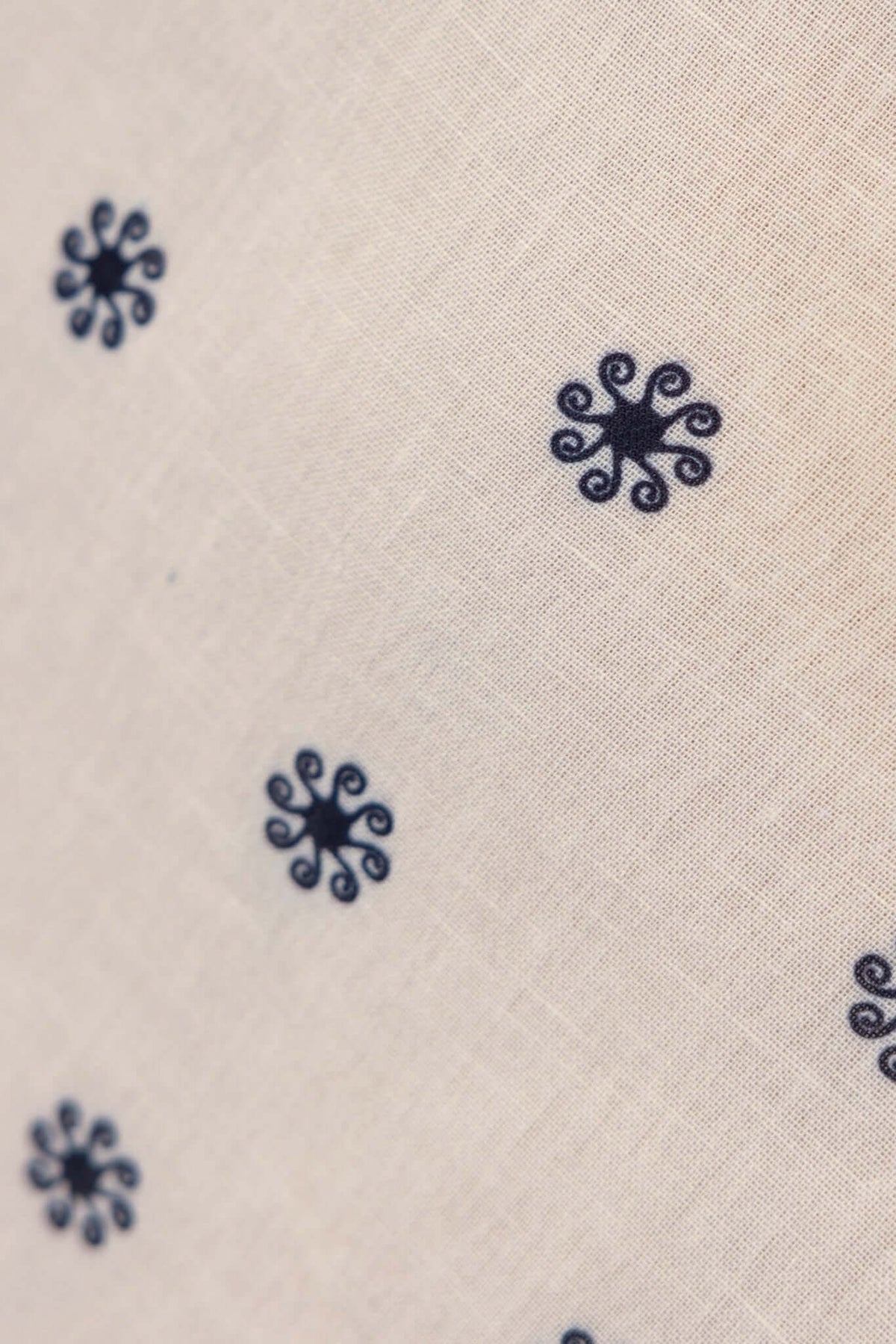 Close-up of patterned fabric featuring small navy blue swirl designs on a light beige background.