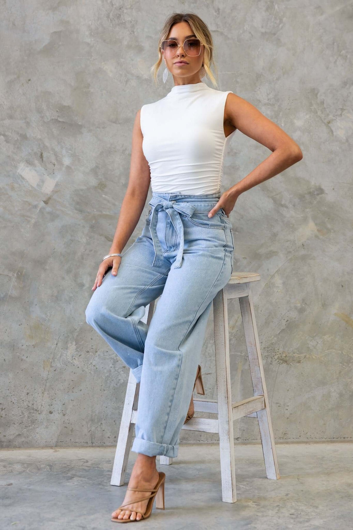 Model wearing Henderson Jeans with a mid-high waist and paper-bag style, paired with a white top and sunglasses.