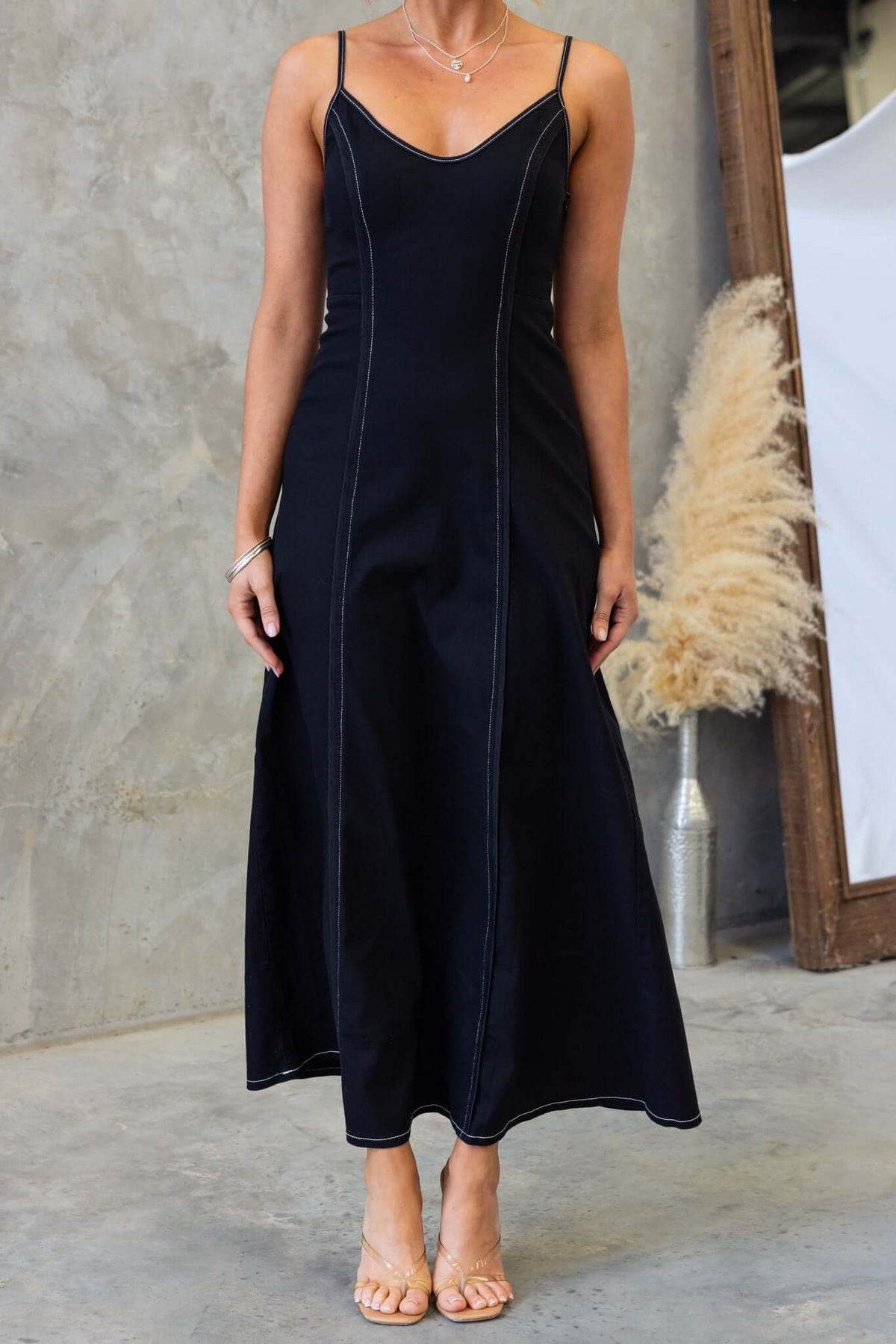 Black denim maxi dress featuring adjustable straps and invisible side zip, modeled with a relaxed fit.