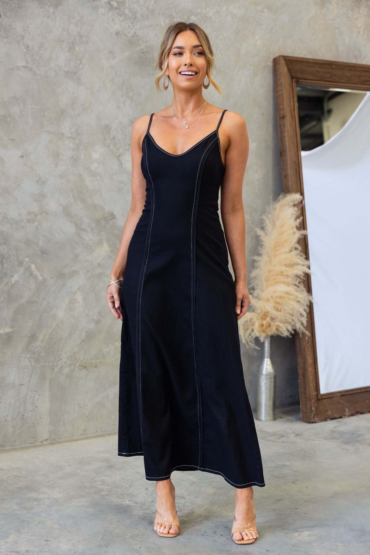 Model wearing a black denim maxi dress with adjustable straps and side zip, styled in a modern setting.