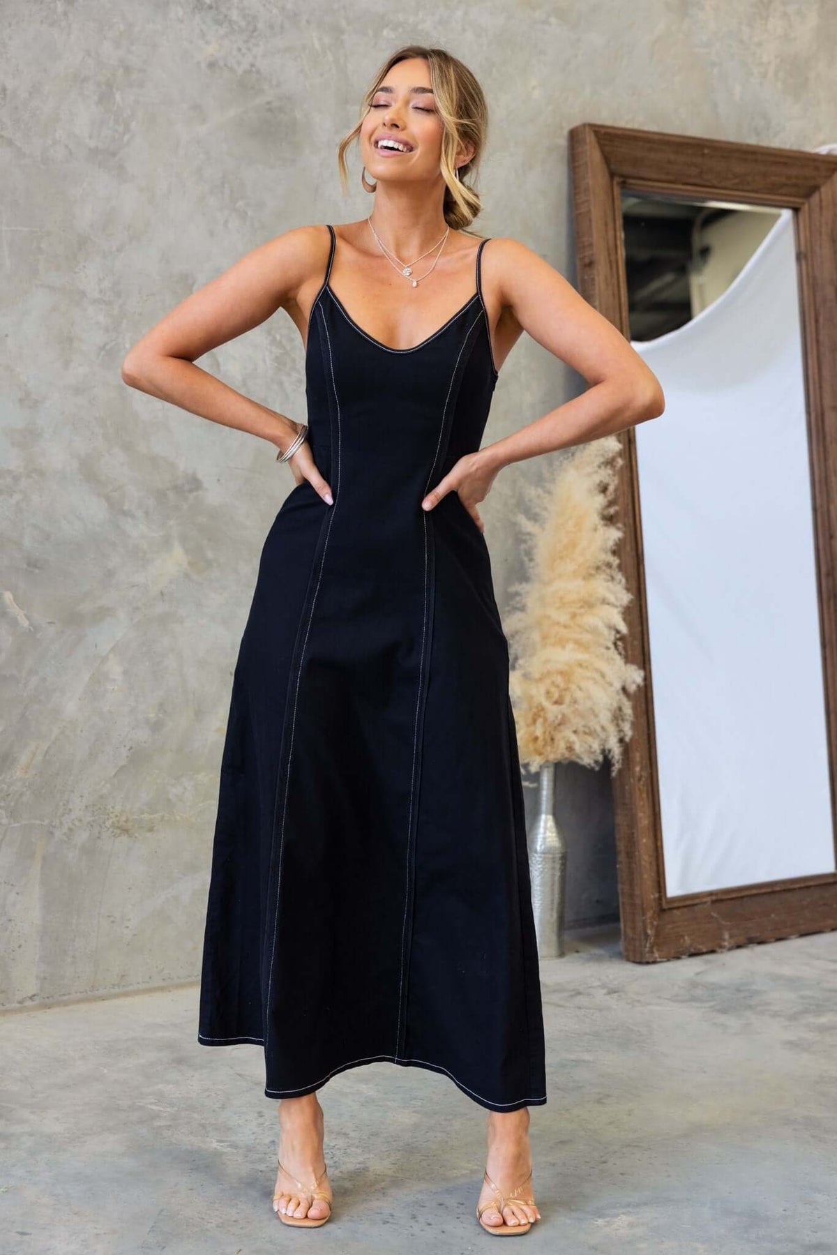 Model wearing a black denim maxi dress with adjustable straps and side zip in a stylish indoor setting.
