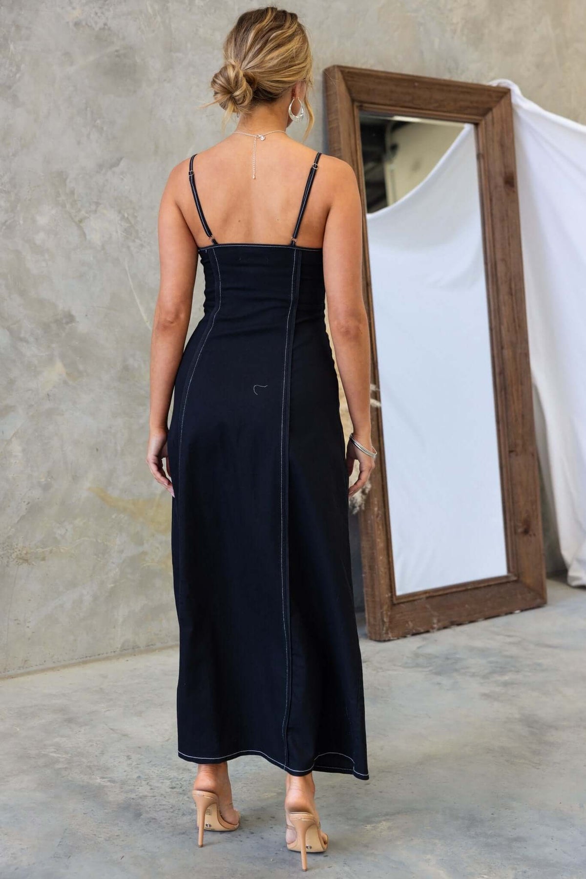 Back view of a black denim maxi dress with adjustable straps and a side zip, styled with a mirror backdrop.