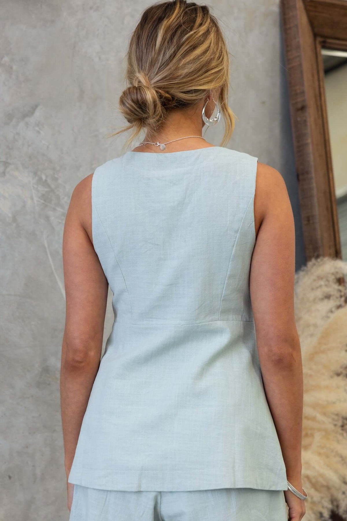 Back view of a woman wearing the Bexley Top, a light blue vest-style top with a fitted design and elegant neckline.