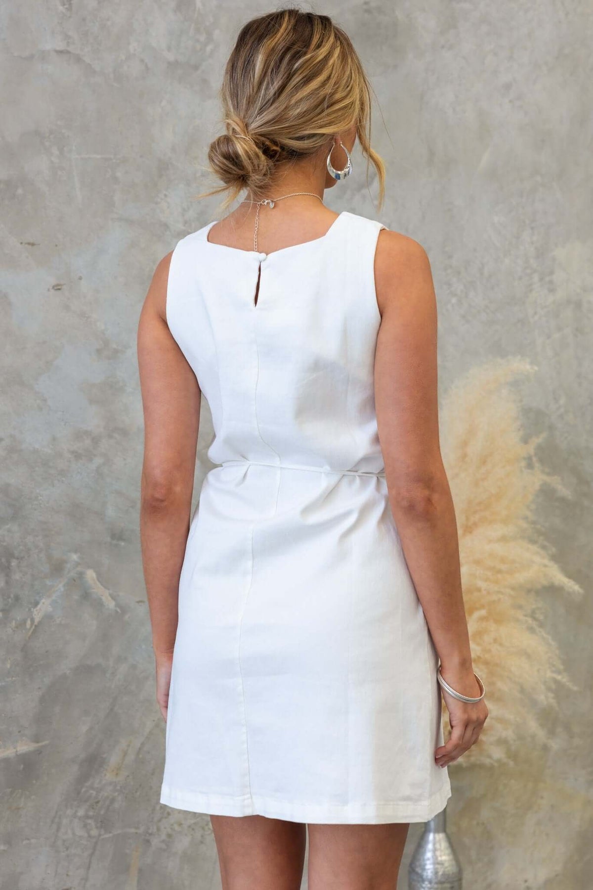 Back view of a woman in a white denim dress showcasing a keyhole detail and relaxed fit, perfect for casual occasions.