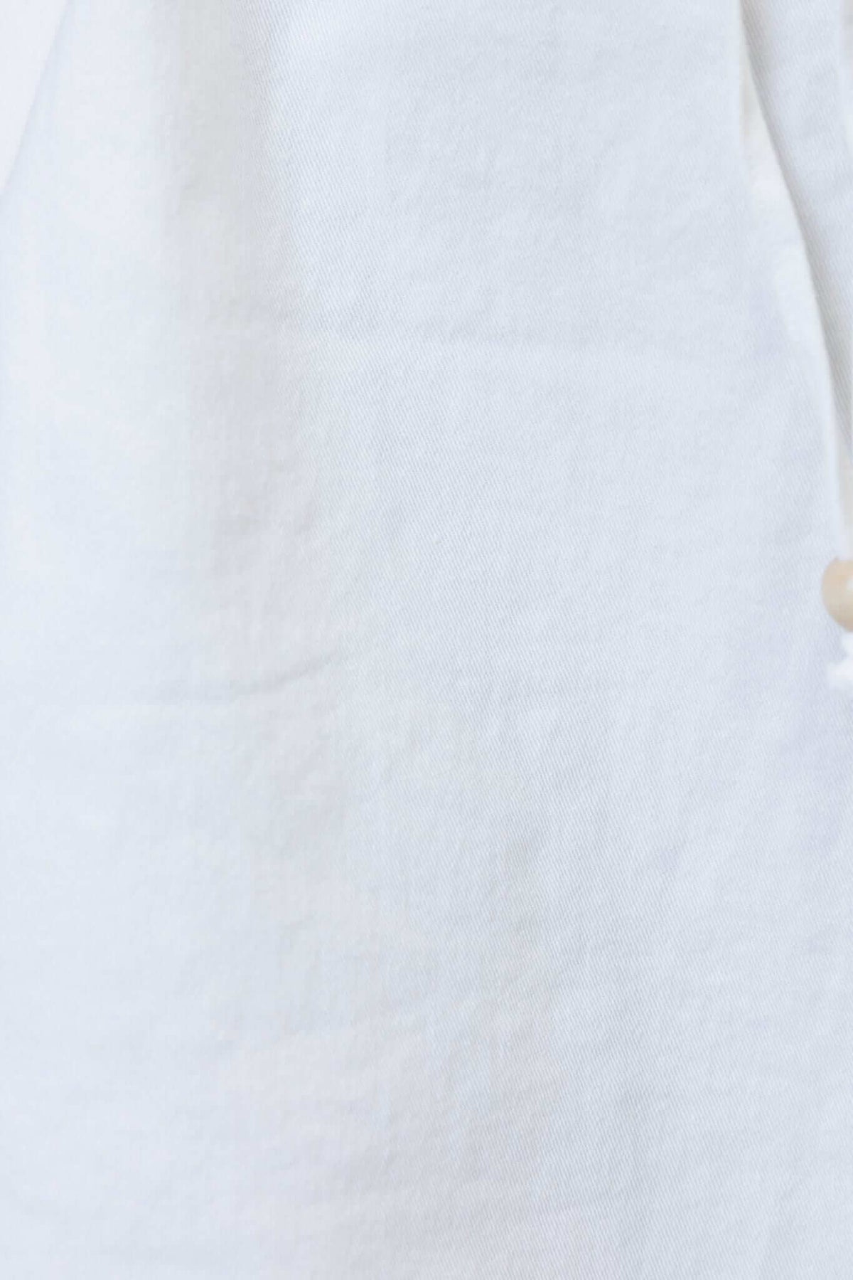 Close-up of white fabric texture with button detail, ideal for showcasing material quality in a fashion product.