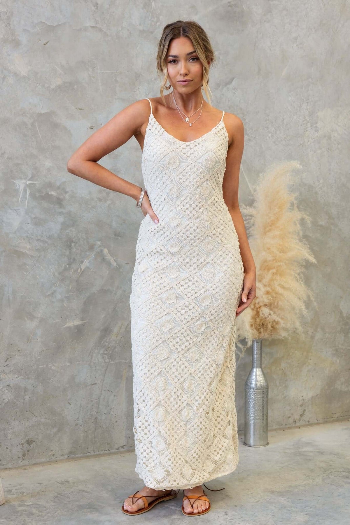 Udele Maxi Dress featuring crochet material, adjustable straps, and a back split, styled in a modern setting.