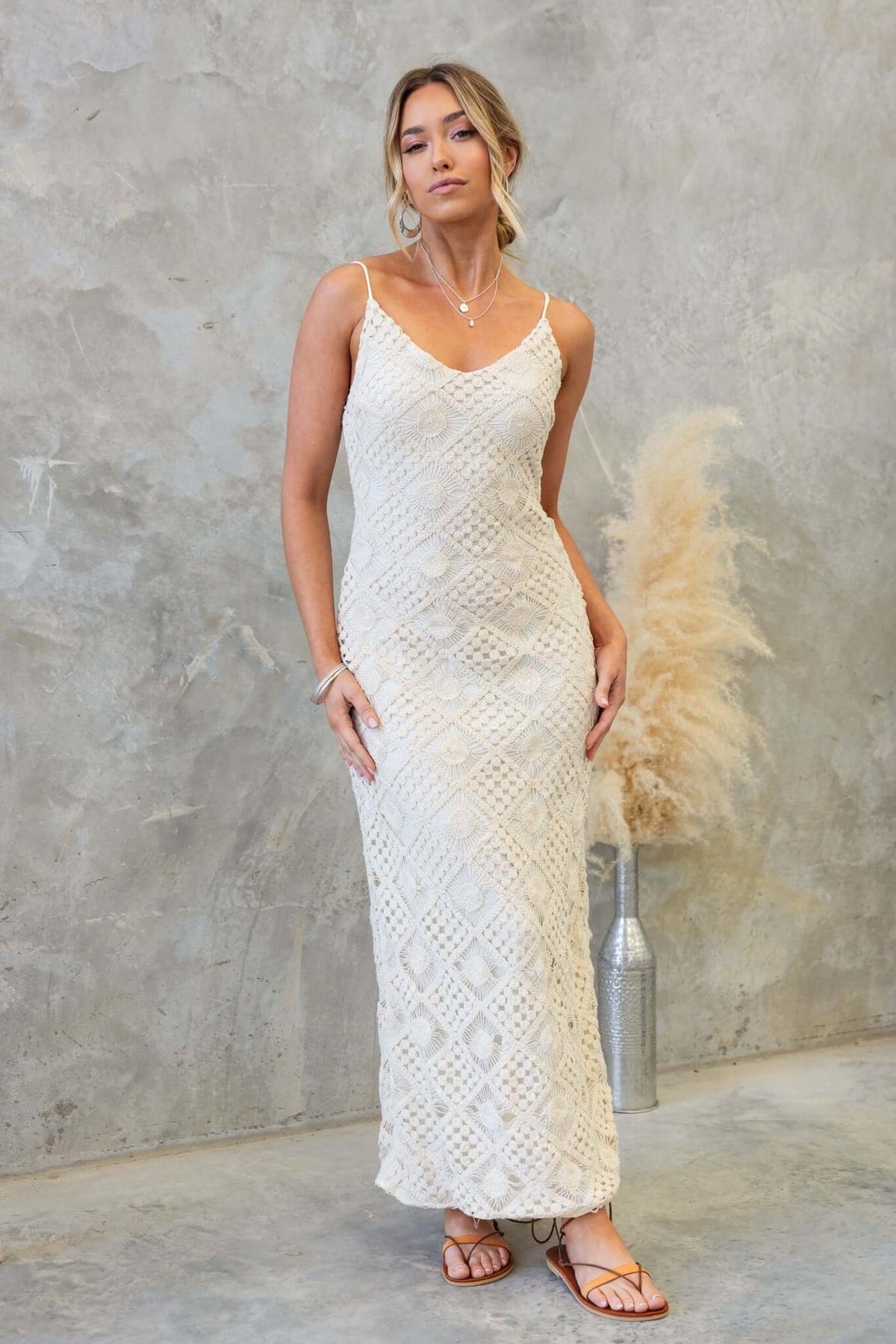 Elegant Udele Maxi Dress in crochet material, featuring adjustable straps and a back split, styled with sandals.