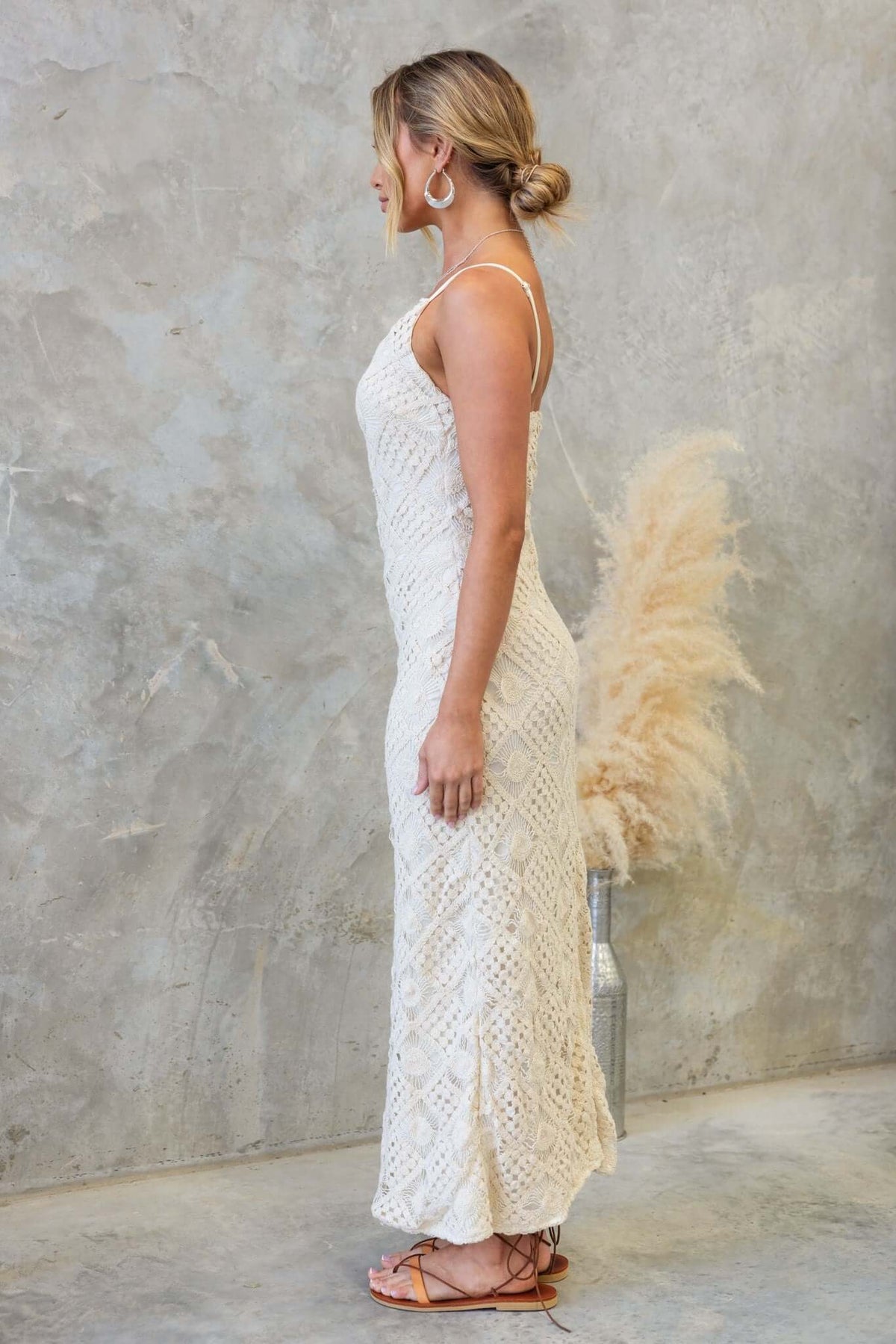 Side view of a woman in a Udele maxi dress, featuring adjustable straps and crochet material, styled with boho decor.