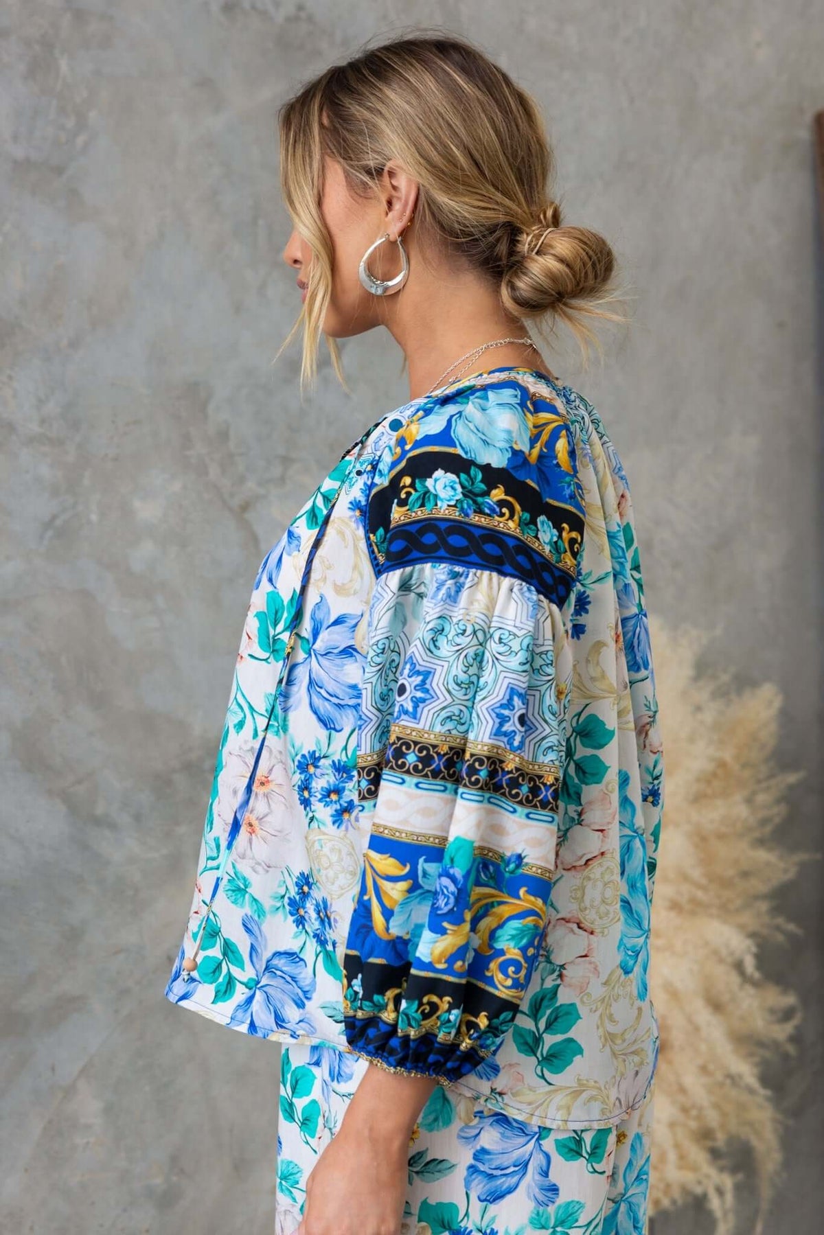 Side view of the Valora Top featuring floral prints, a V-neckline, and tie detail, styled with hoop earrings.