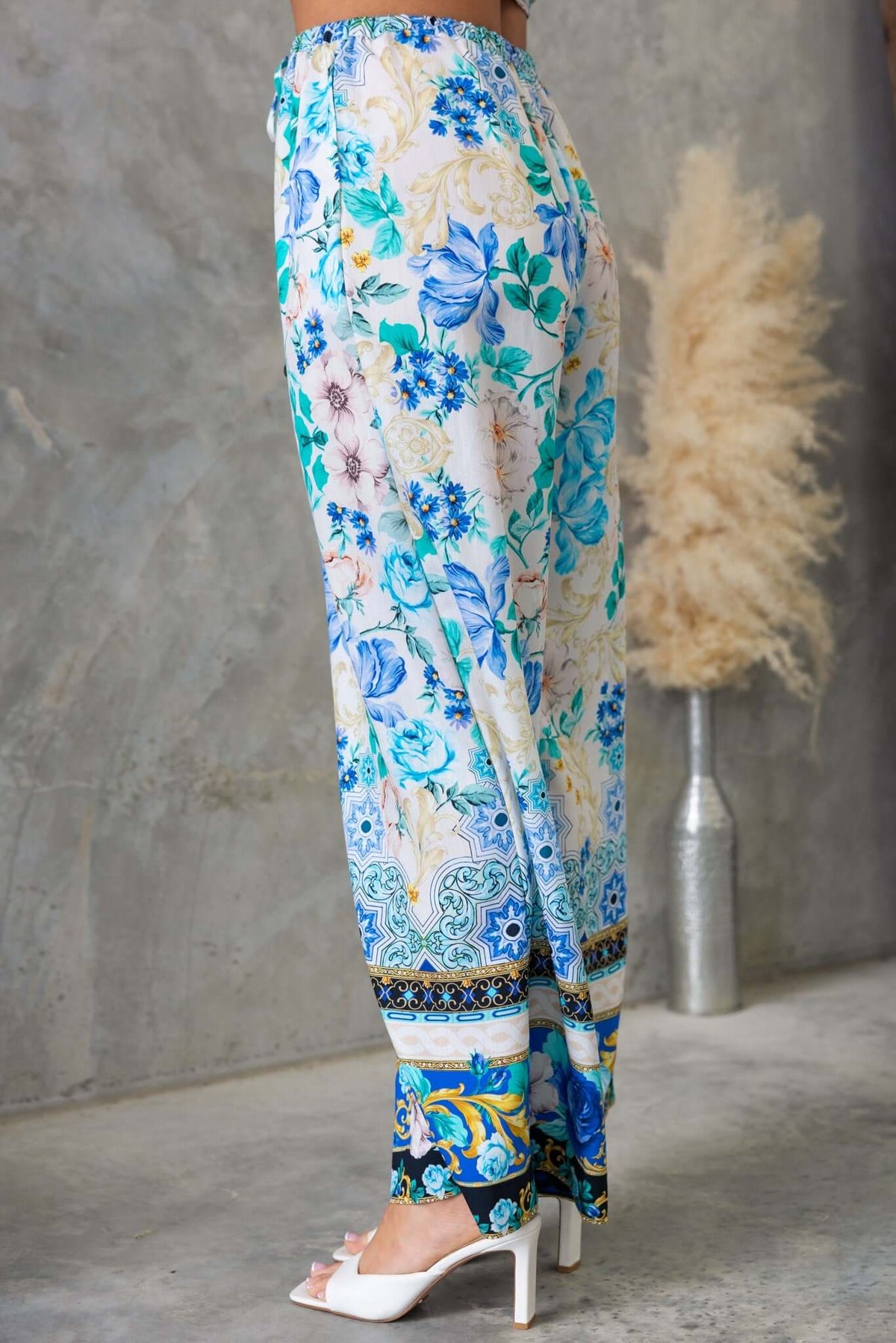 Valora Pants in floral print, featuring high waist, elastic waistband, and pockets, styled with white heels.