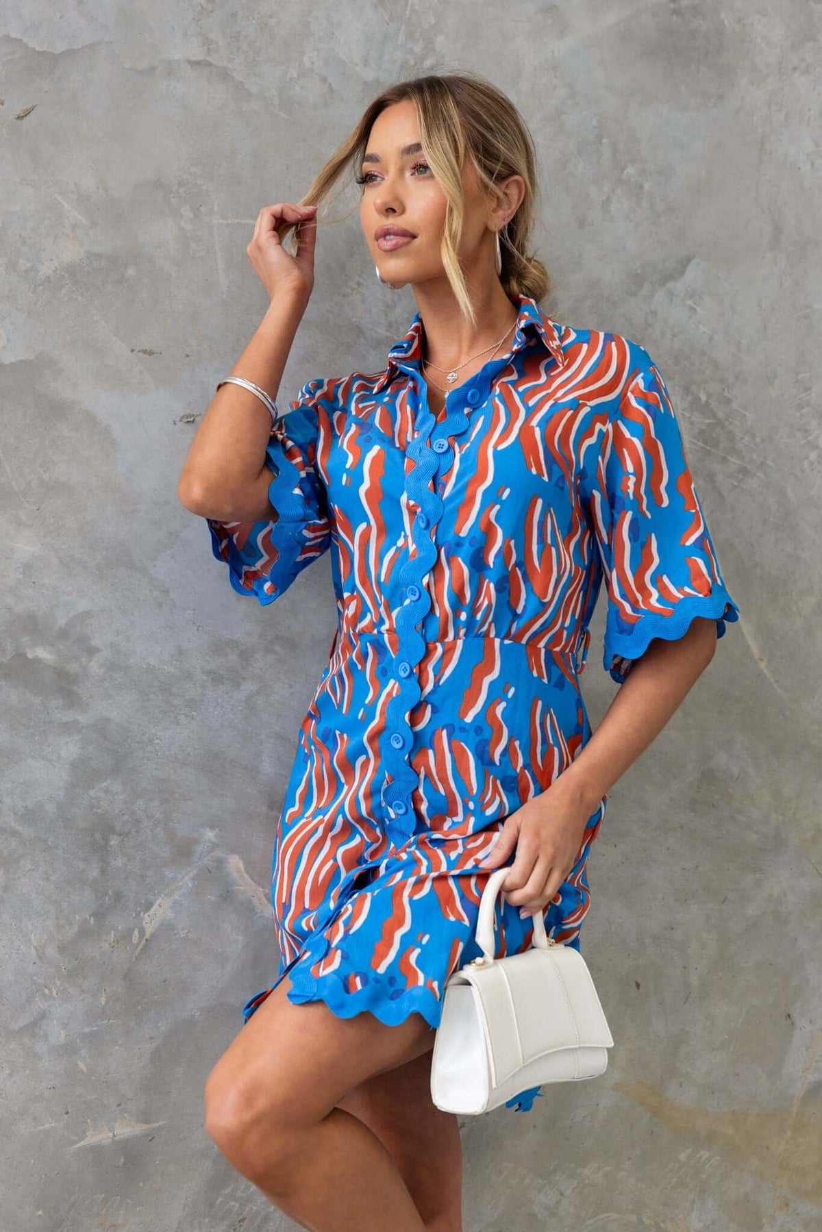 Model wearing Alfonzo Dress with vibrant blue and red patterns, featuring a button-up front and removable belt.