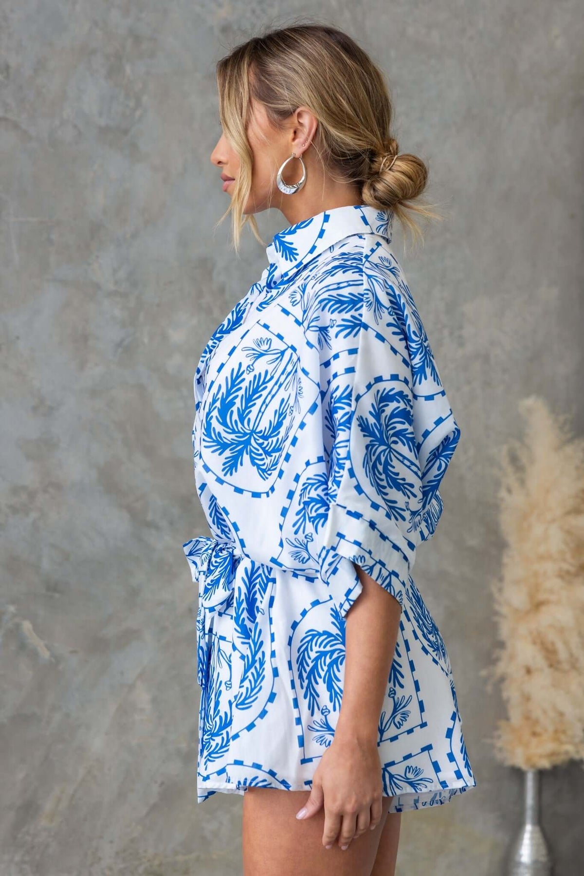 Side view of the Alli Playsuit featuring a blue and white palm print, collar, and button-up design.