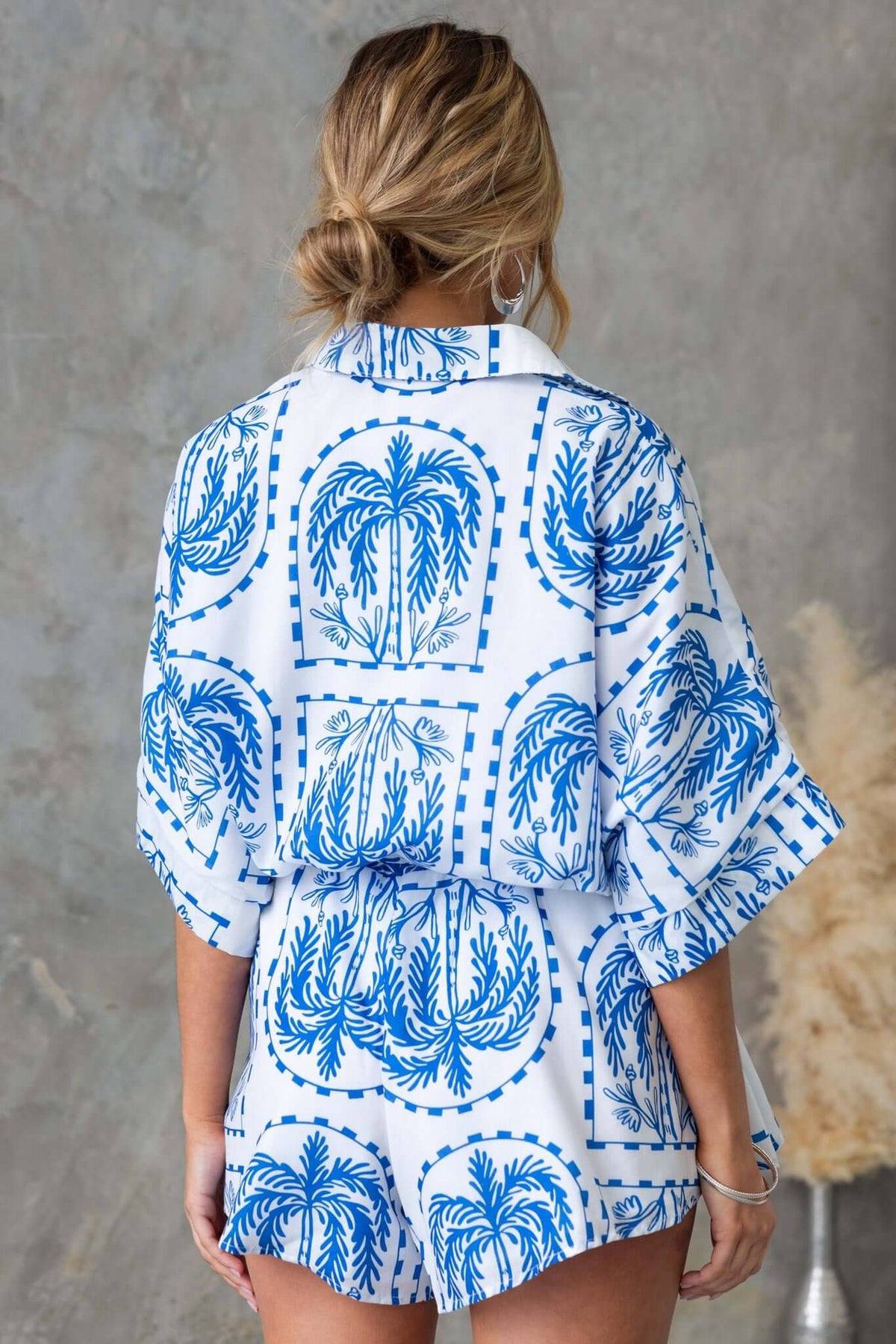 Back view of Alli Playsuit featuring a blue and white palm print, with a relaxed fit and button-up collar.