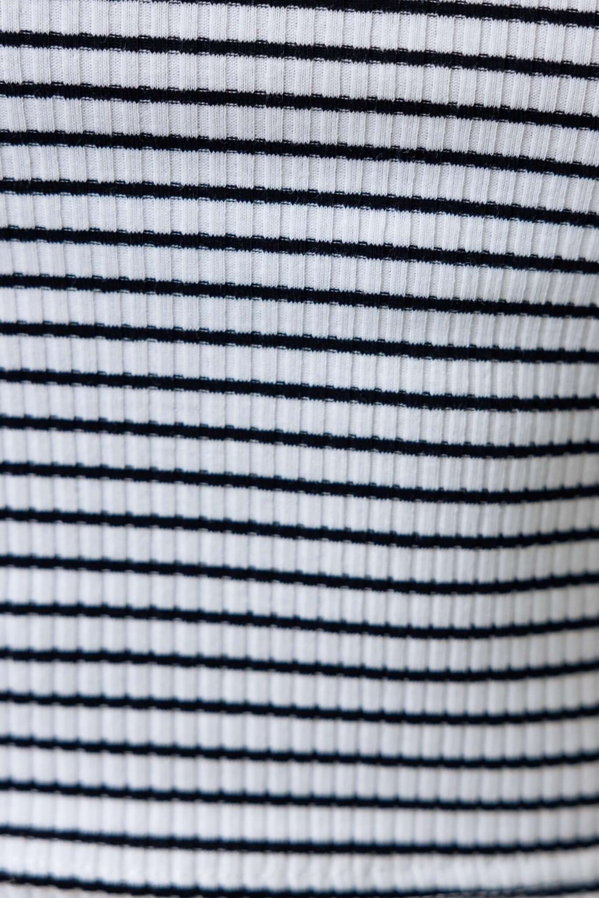 Close-up of ribbed knit fabric featuring alternating black and white stripes, showcasing texture and stretch of the material.