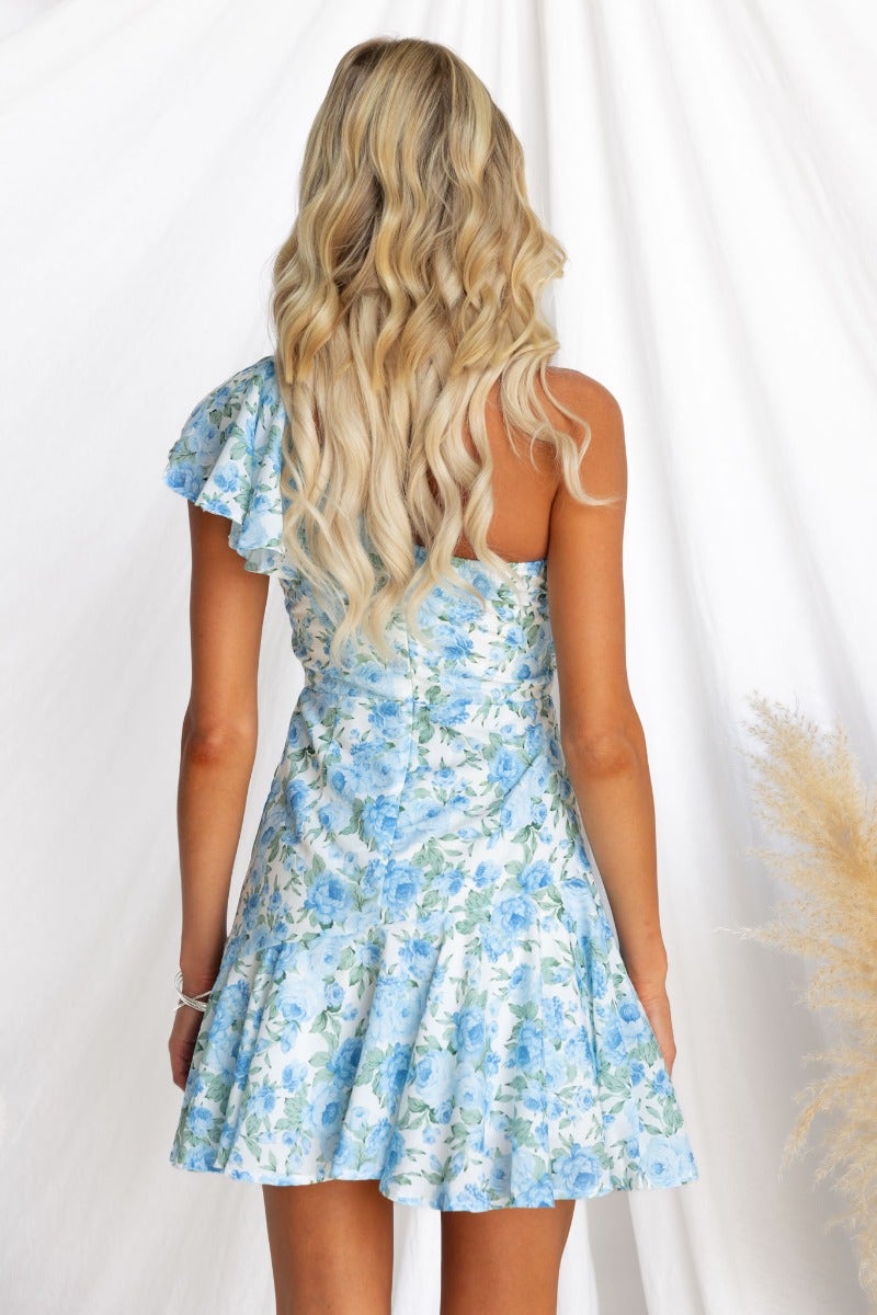 Back view of Uze Dress featuring a one-shoulder neckline, floral print, and flared skirt in light blue tones.