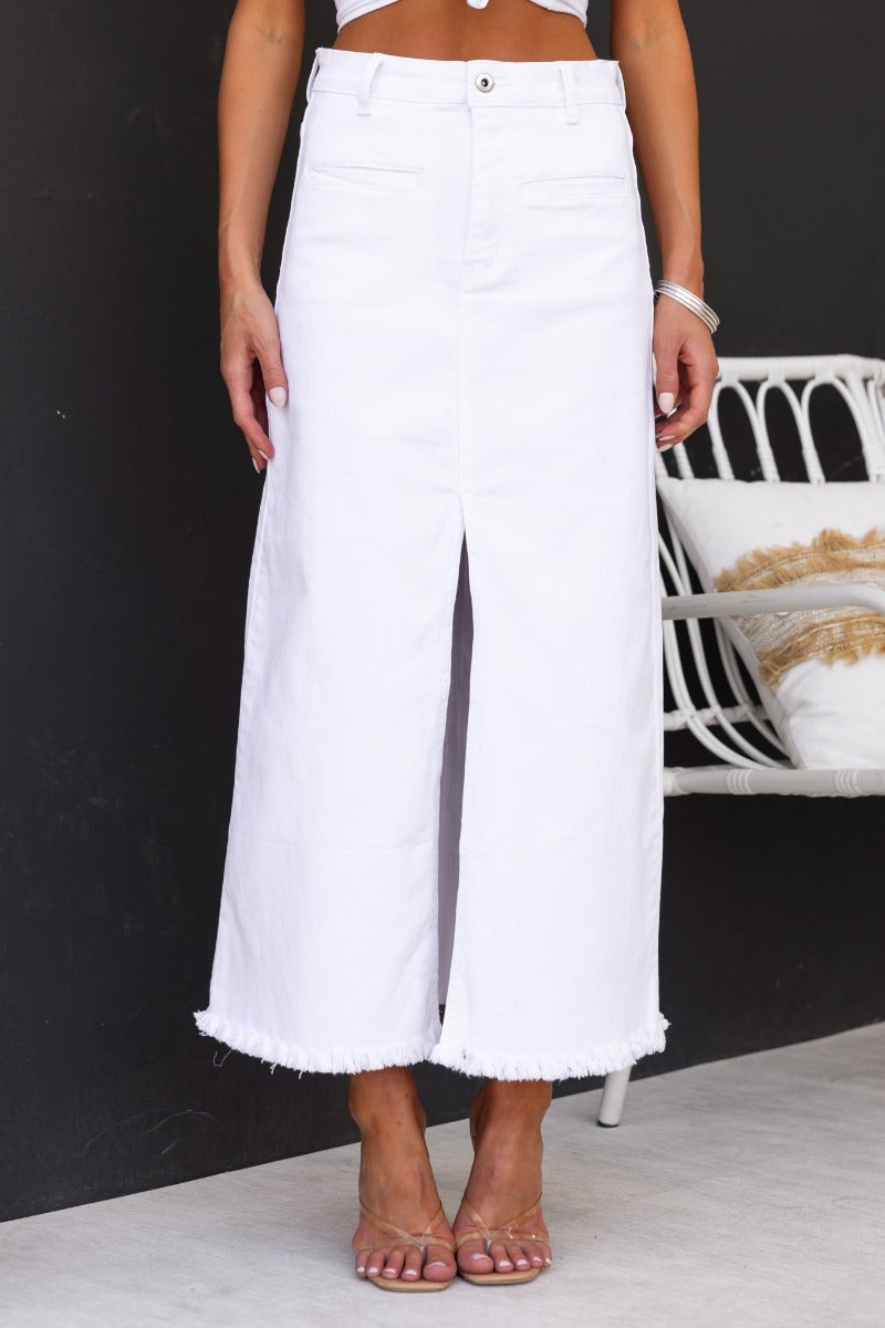 White denim maxi skirt with front split and frayed hem, styled with a cropped top.