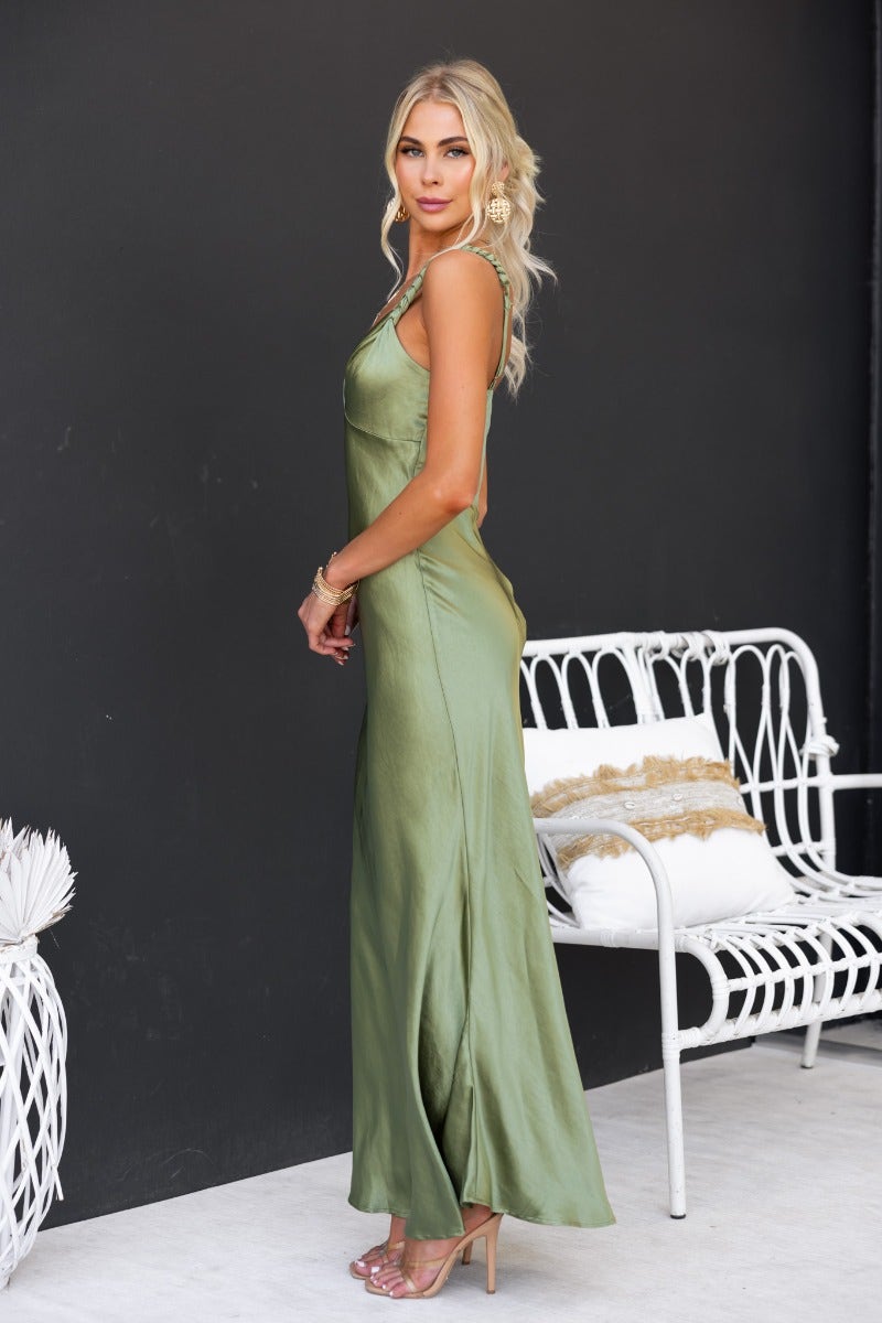 Model wearing a Forest Maxi Dress in green satin, with adjustable straps and a fitted silhouette, styled elegantly against a dark background.