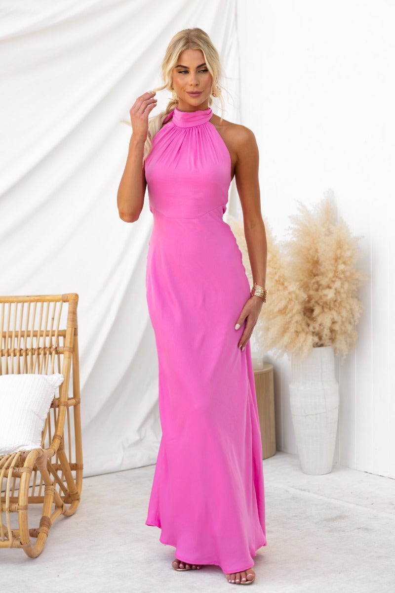 Model wearing a pink maxi dress with a high tie neckline and a slight sheen, posed against a neutral backdrop.