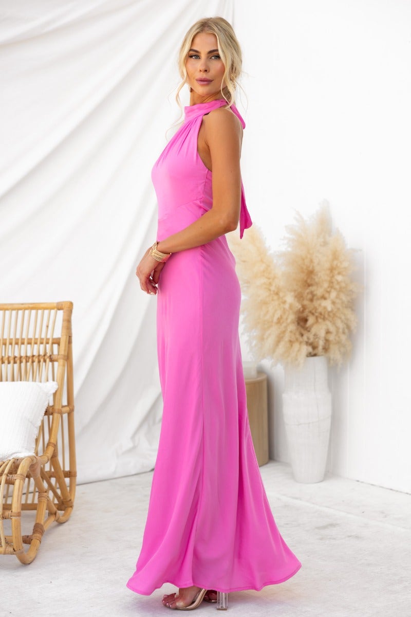Model showcasing the Forbidden Love Maxi Dress in bright pink, featuring a high tie neckline and flowing silhouette.