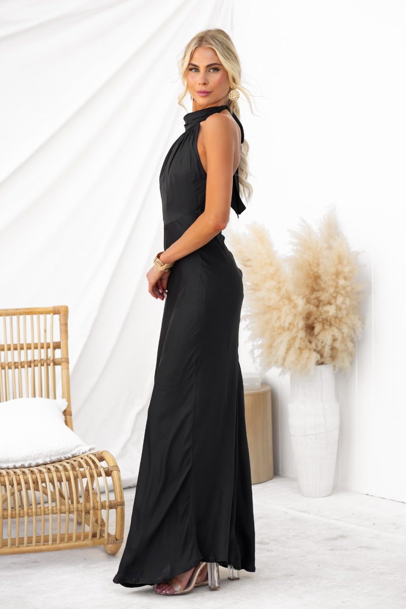 Model in a sleek black maxi dress with high tie neckline, showcasing a slight sheen and elegant fit.