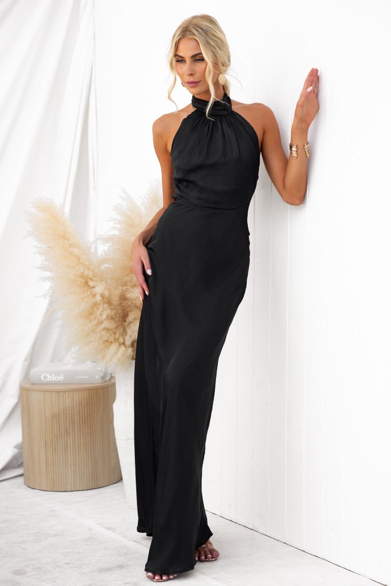 Model wearing the Forbidden Love Maxi Dress in black with high tie neckline and a slight sheen, styled elegantly.