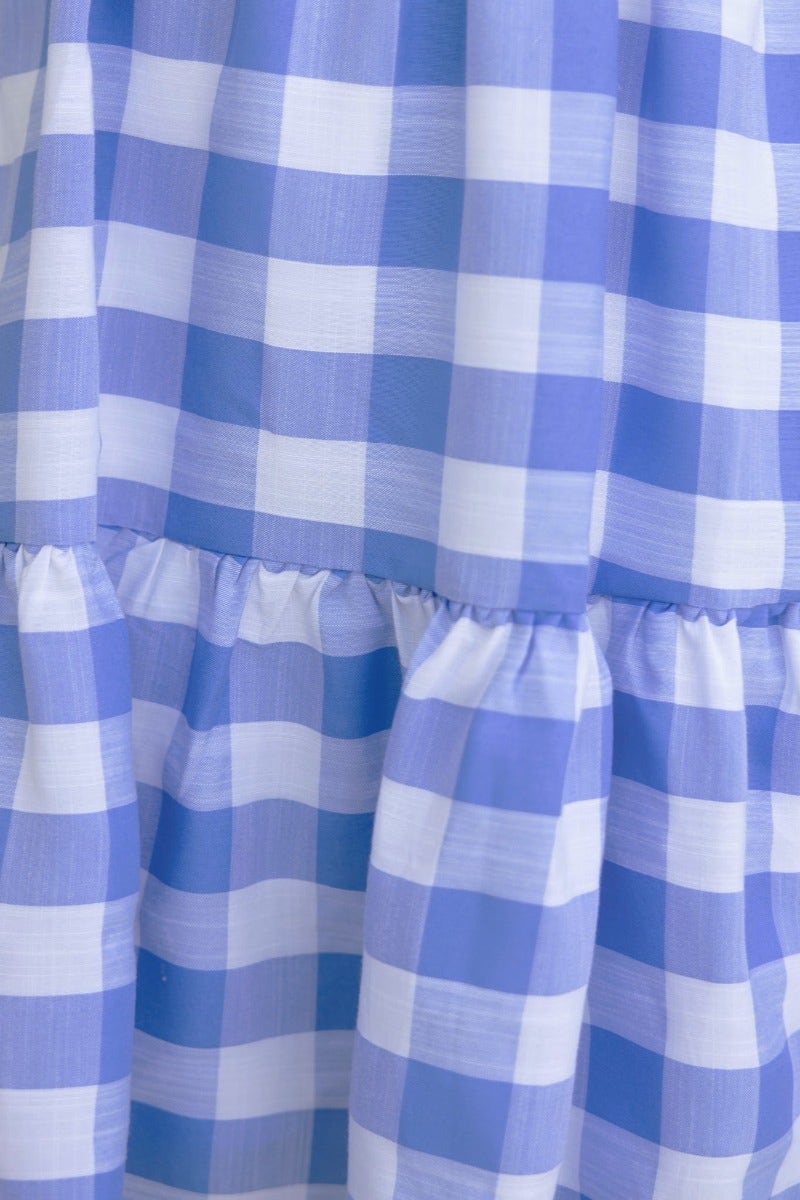 Close-up of blue and white plaid dress fabric with gathered detailing, showcasing light cotton material and stylish pattern.