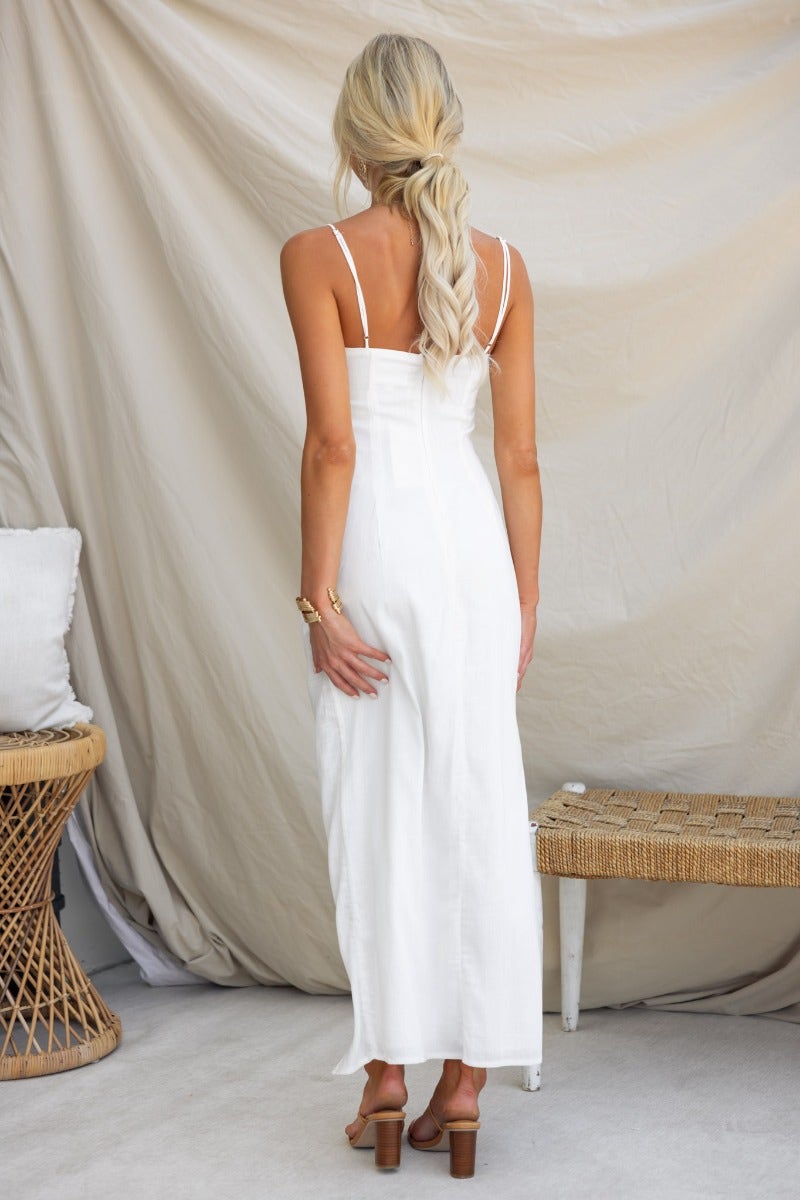 Back view of a woman wearing a white Beloved Midi Dress with adjustable straps and tie skirt, showcasing its linen texture.