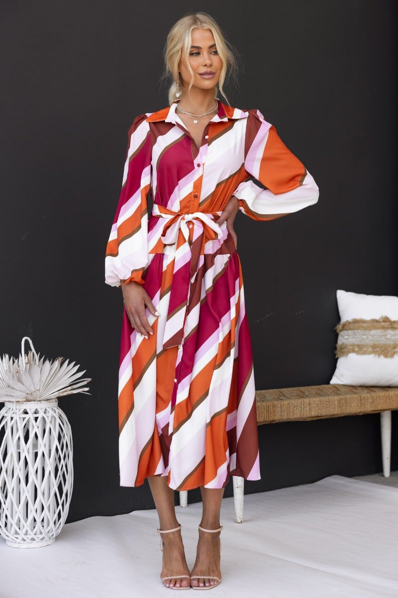 Nylah Midi Dress in multi-colour stripes, button-up front, with removable belt and elastic cuffs, styled with strappy heels.