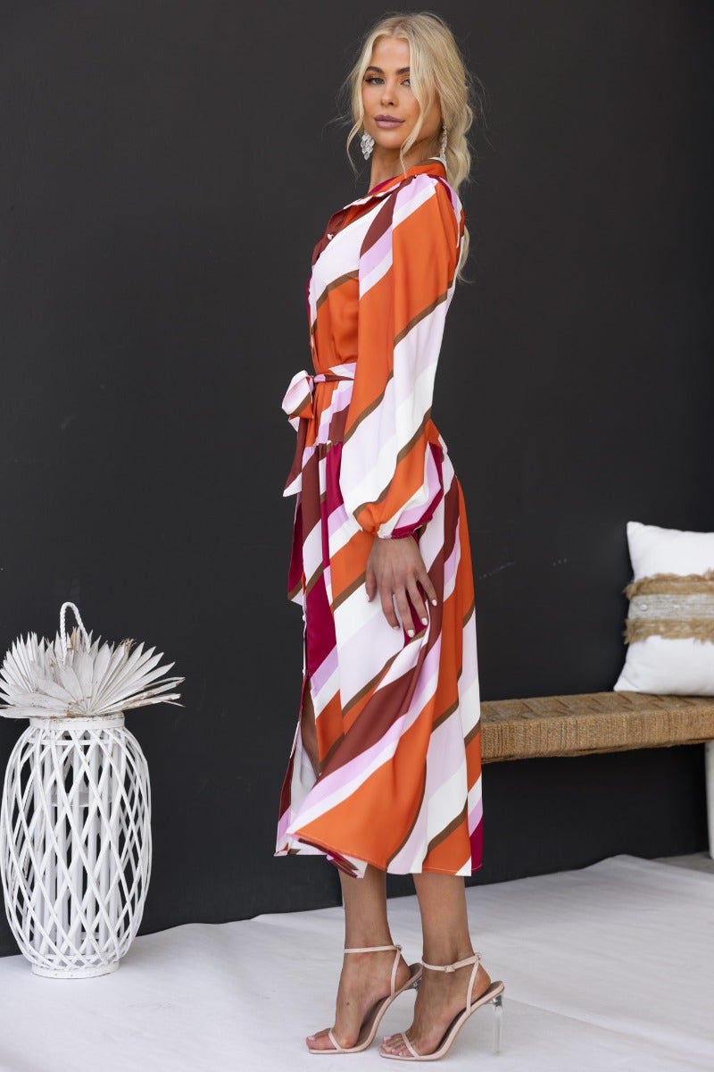 Profile view of Nylah Midi Dress with multi-colour stripes, removable belt, and elastic cuffs, worn by a model in stylish setting.
