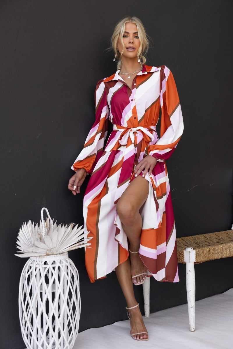 Model wearing Nylah Midi Dress, a colorful striped button-up dress with a removable belt and elastic cuffs.