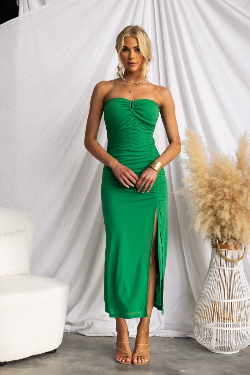 Model wearing a strapless green Hidden Hills midi dress with ruching and a front split.