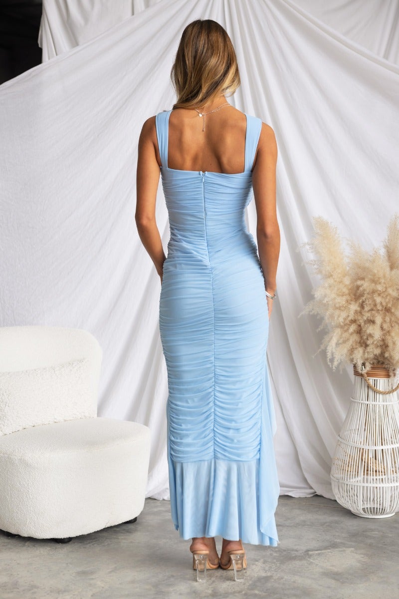 Model wearing a light blue Moscato maxi dress with a ruched design and high-low hemline, standing against a white backdrop.