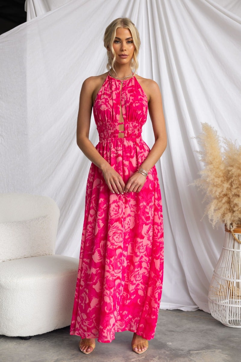 Model wearing Kariah Maxi Dress in vibrant pink with floral pattern, adjustable halter neckline, and elastic waistband.
